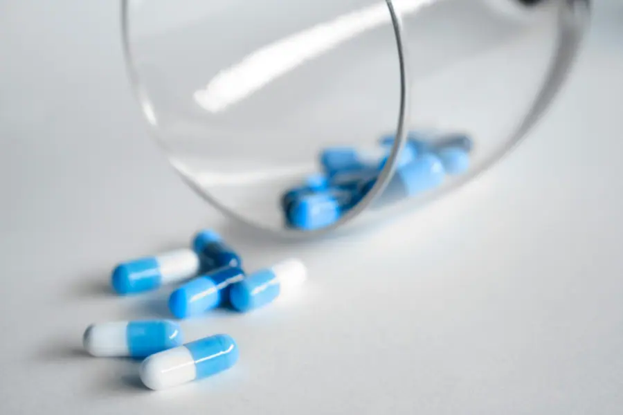 Capsule bianche e blu che fuoriescono da un contenitore di vetro